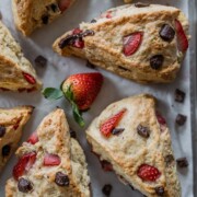 Frisch gebackene Scones mit Schokoladenstückchen und Erdbeerstückchen, angerichtet auf Pergamentpapier mit einer ganzen Erdbeere in der Mitte. Diese goldbraunen Scones sind weich, flockig und perfekt für alle, die ein leckeres Scones-Rezept suchen.