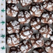 Ein Tablett gefüllt mit American Chocolate Crinkle Cookies, die mit Puderzucker bestäubt sind, um einen Crack-Effekt zu erzielen. Der Rand des Tabletts wird von einem festlichen Tuch mit grünen Sternen eingefasst - das perfekte Weihnachtsplätzchen für die Weihnachtszeit.