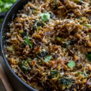 Eine Nahaufnahme eines gebackenen Auflaufs in einer schwarzen Schale mit Reis, Brokkoli, Käse und karamellisierten Zwiebeln, garniert mit frischen Korianderblättern - perfekt als schnelles Mittagessen für alle, die schnelle Rezepte lieben. Die Oberfläche ist goldbraun und knusprig.