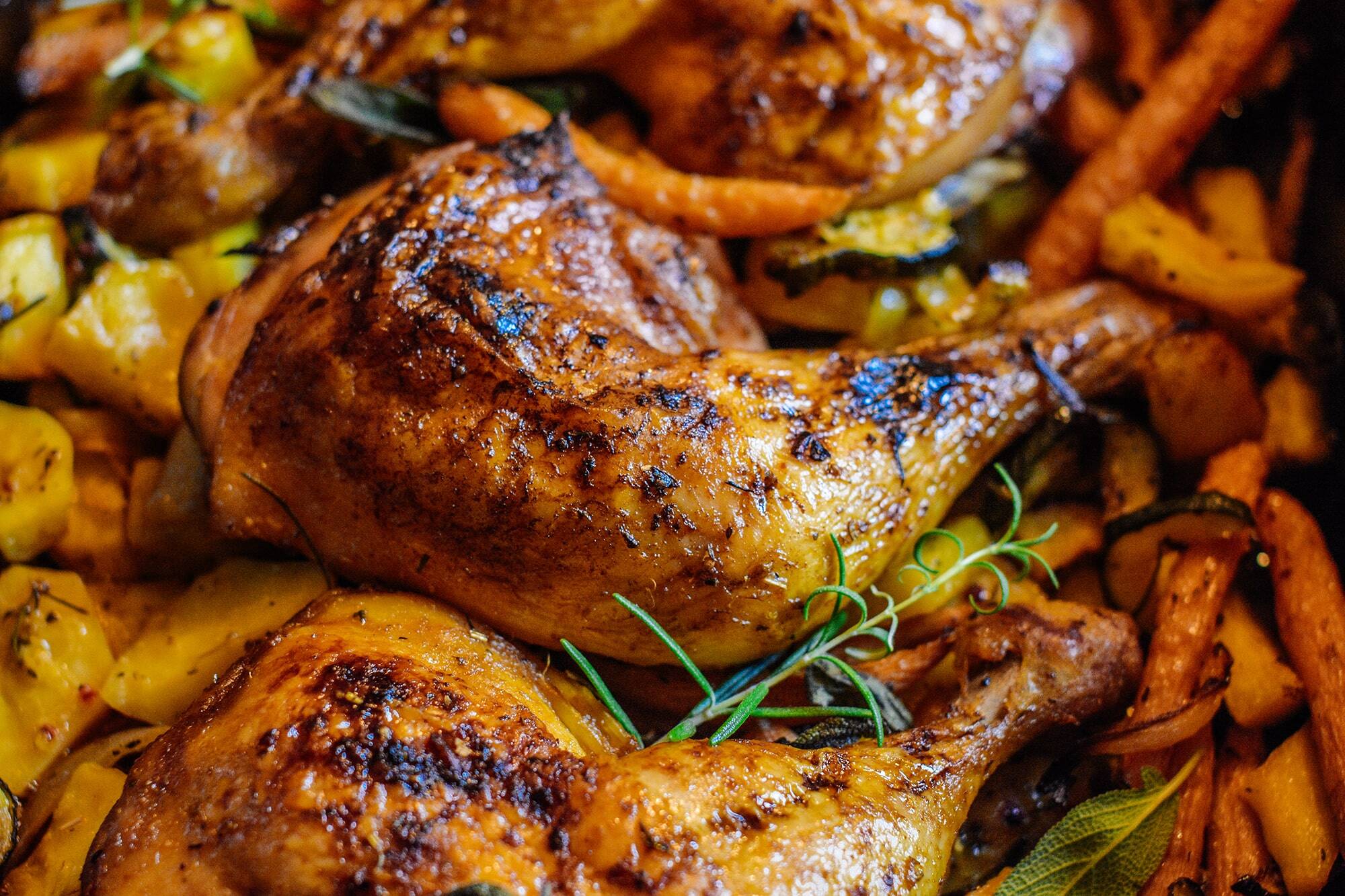 Knusprige Hähnchenschenkel mit goldener Haut, umgeben von im Ofen gerösteten Karotten, Kartoffeln und Zucchini, garniert mit frischem Rosmarin und Salbei. Entdecke köstliche Hähnchenschenkel im Backofen für ein unwiderstehliches Aroma!.