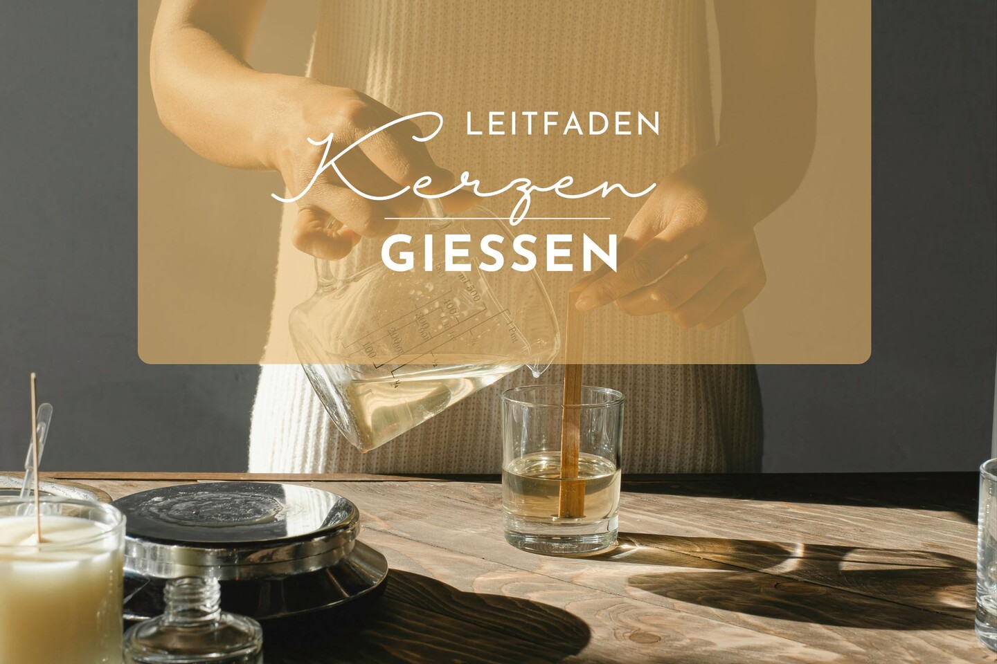 Eine Person gießt geschmolzenes Wachs aus einem Glasbehälter in ein Glas mit einem Kerzenhalter auf einem Holztisch. Der überlagerte Text in Deutsch lautet: Leitfaden Kerzen Giessen.