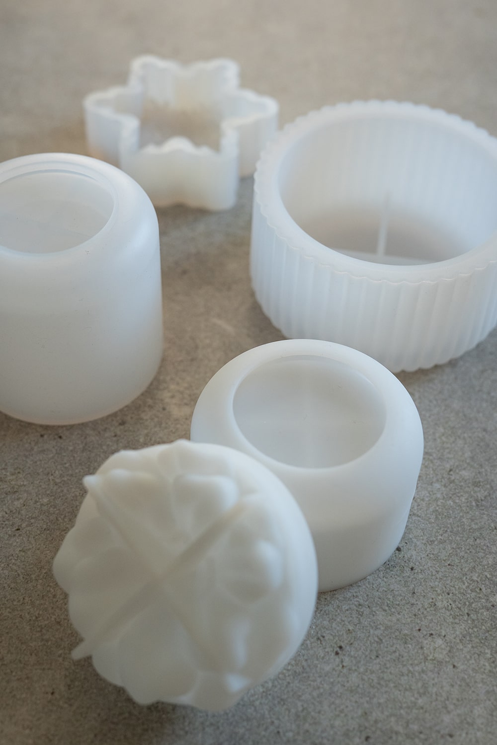 Mehrere weiße Kunststoffformen unterschiedlicher Form und Größe, darunter eine runde, geriffelte Form, eine runde Form mit Querschnitt und ein schmetterlingsförmiger Ausstecher, sind auf einer grauen Fläche angeordnet.