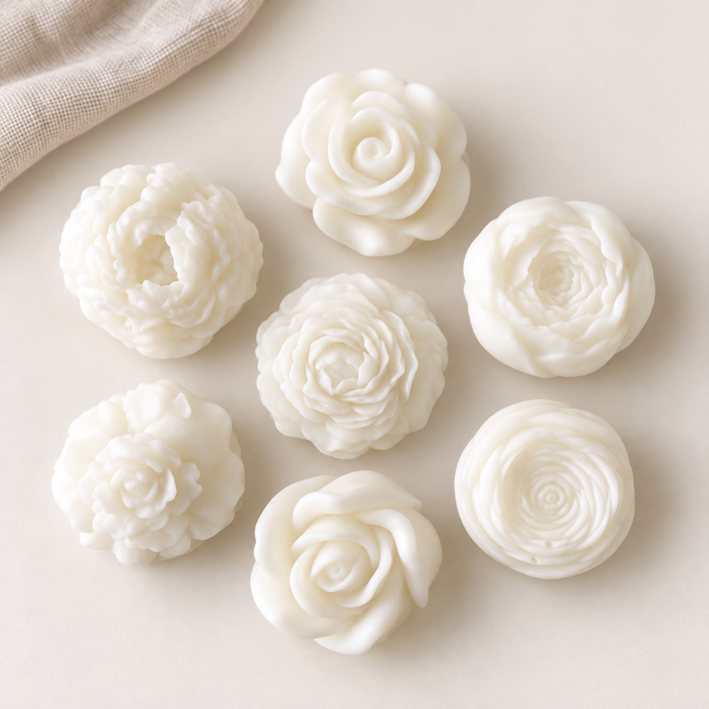 Sieben weiße, blumenförmige, handgefertigte Duftwachsmelt-Stücke, auf einer neutralen Unterlage angeordnet.
